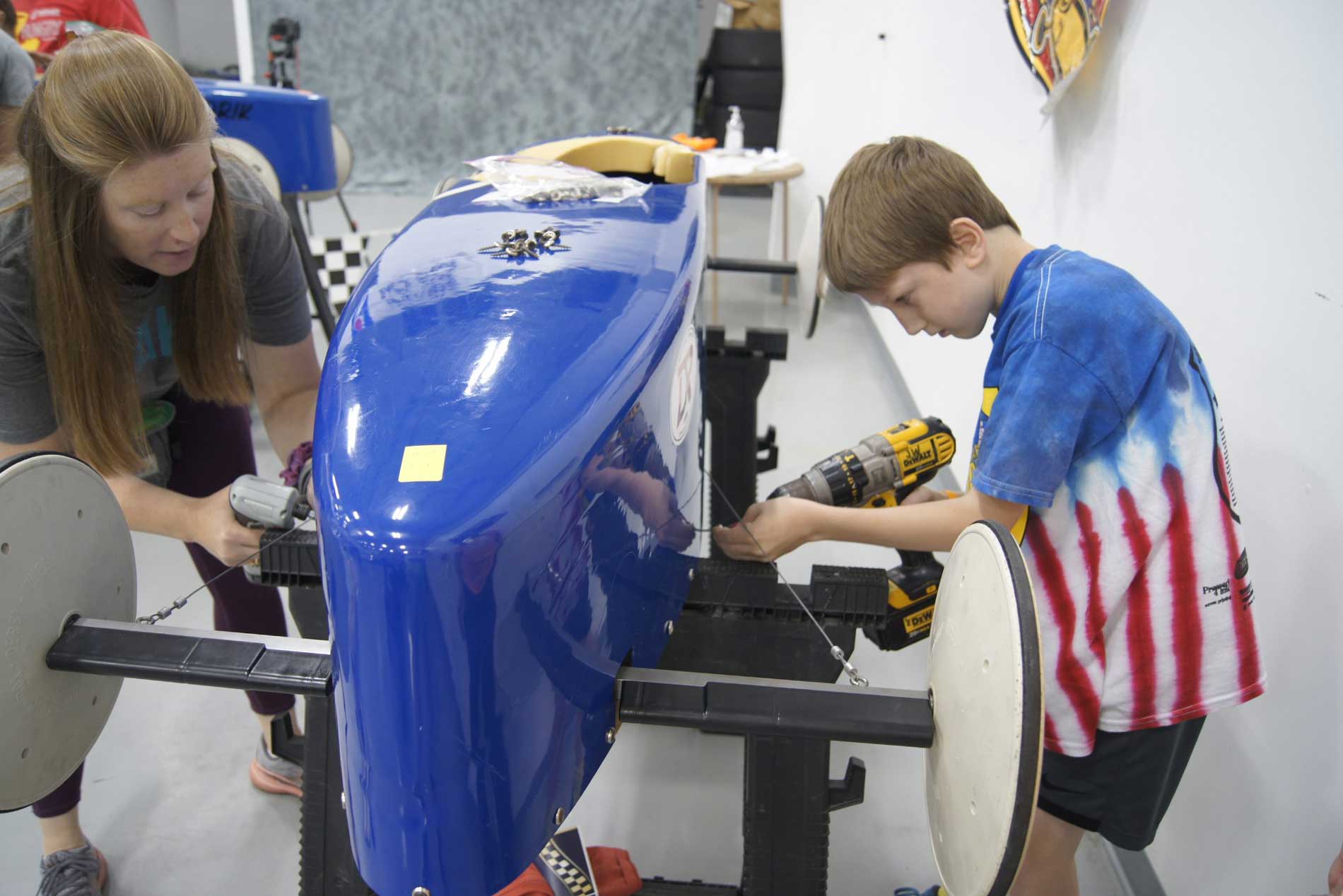 Young kid and instructor working on a blue derby car